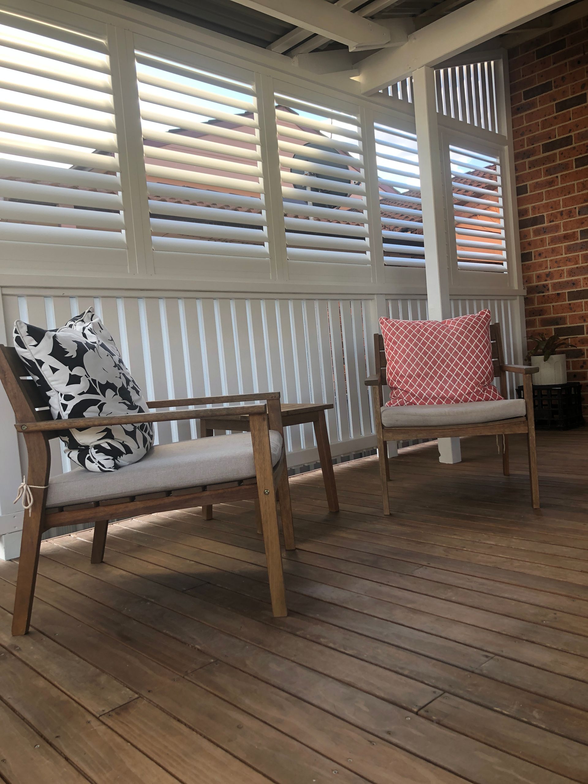 Two Wooden Chairs With Cushions Sit on a Wooden Deck. Blinds and a Brick Wall Are in the Background — My Timber Flooring Blinds & Shutters in Erina, NSW