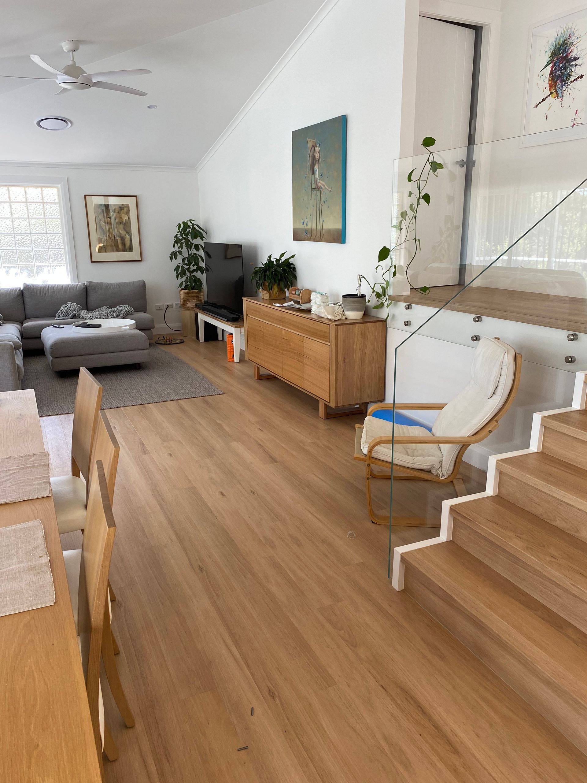 Living Room With Wood Floors, Sofa, Wood Cabinet, Stairs, and Artwork — My Timber Flooring Blinds & Shutters in Erina, NSW