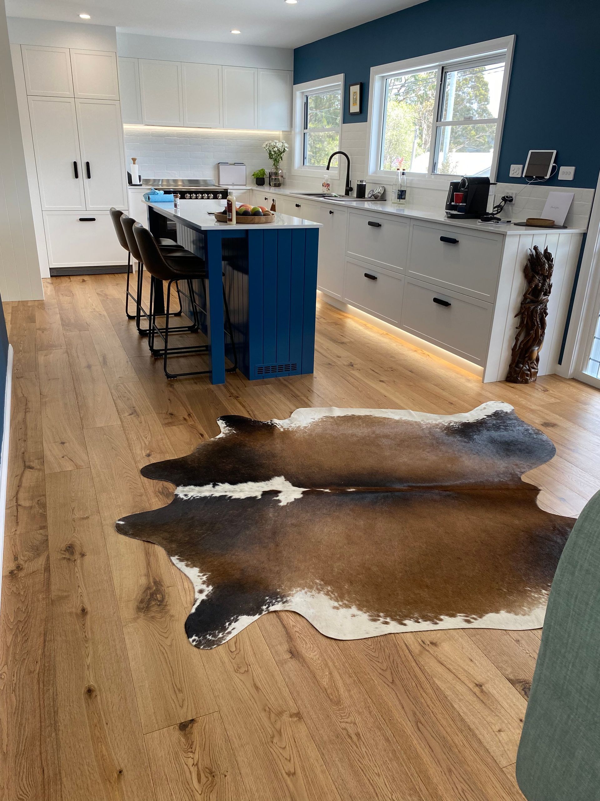 Cowhide rug on wood floor in a modern kitchen with a blue island and white cabinets. — My Timber Flooring Blinds & Shutters in Erina, NSW