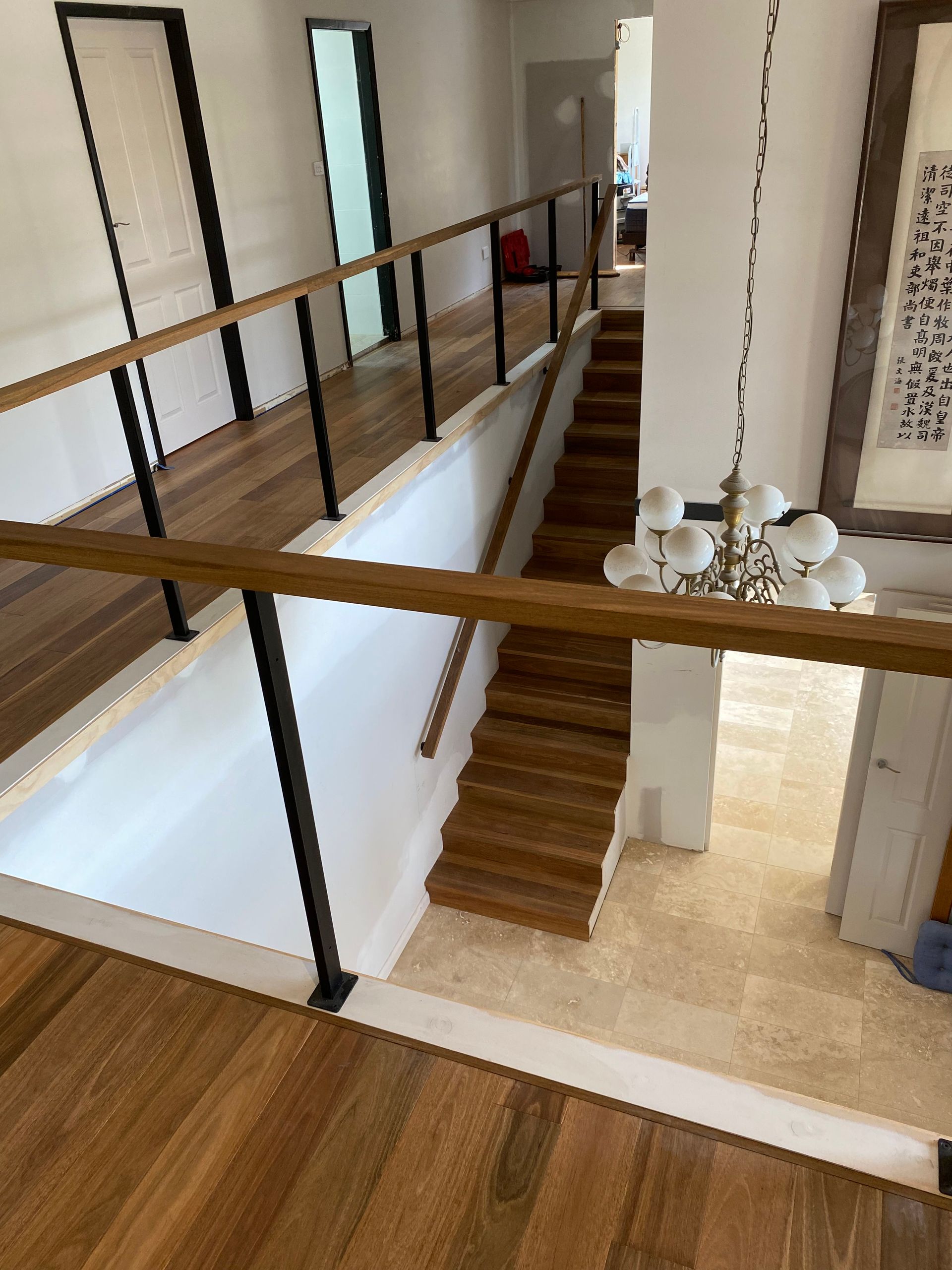 Wooden Staircase and Balcony With Black Railing and Chandelier — My Timber Flooring Blinds & Shutters in Erina, NSW