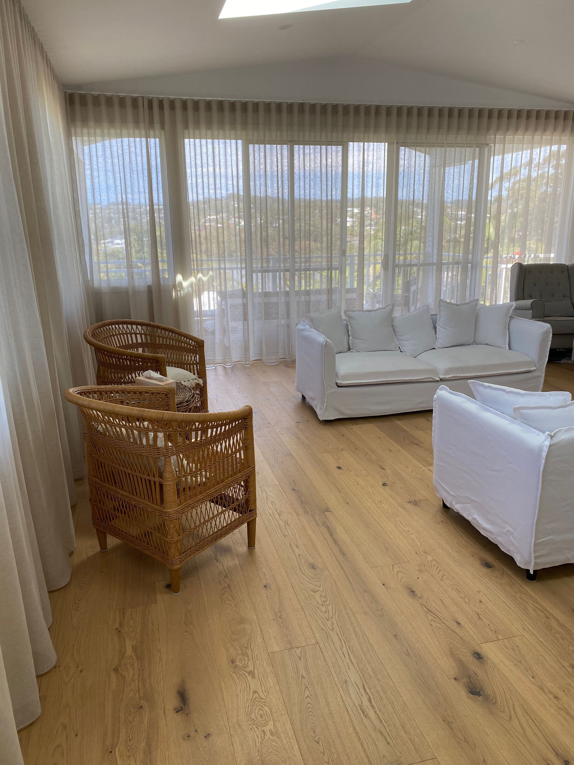 Bright Living Room With Woven Chairs, White Couches and Sheer Curtains Over Large Windows — My Timber Flooring Blinds & Shutters in Erina, NSW