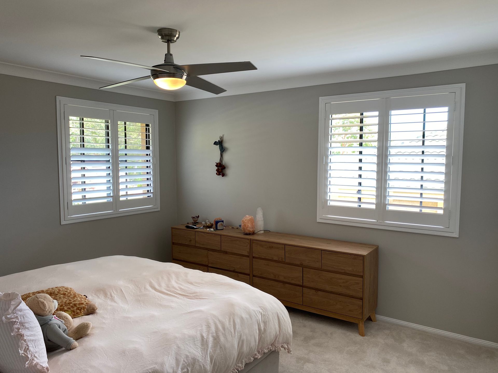 Bedroom With a Wooden Dresser, Two Windows With White Shutters, and a Ceiling Fan — My Timber Flooring Blinds & Shutters in Erina, NSW