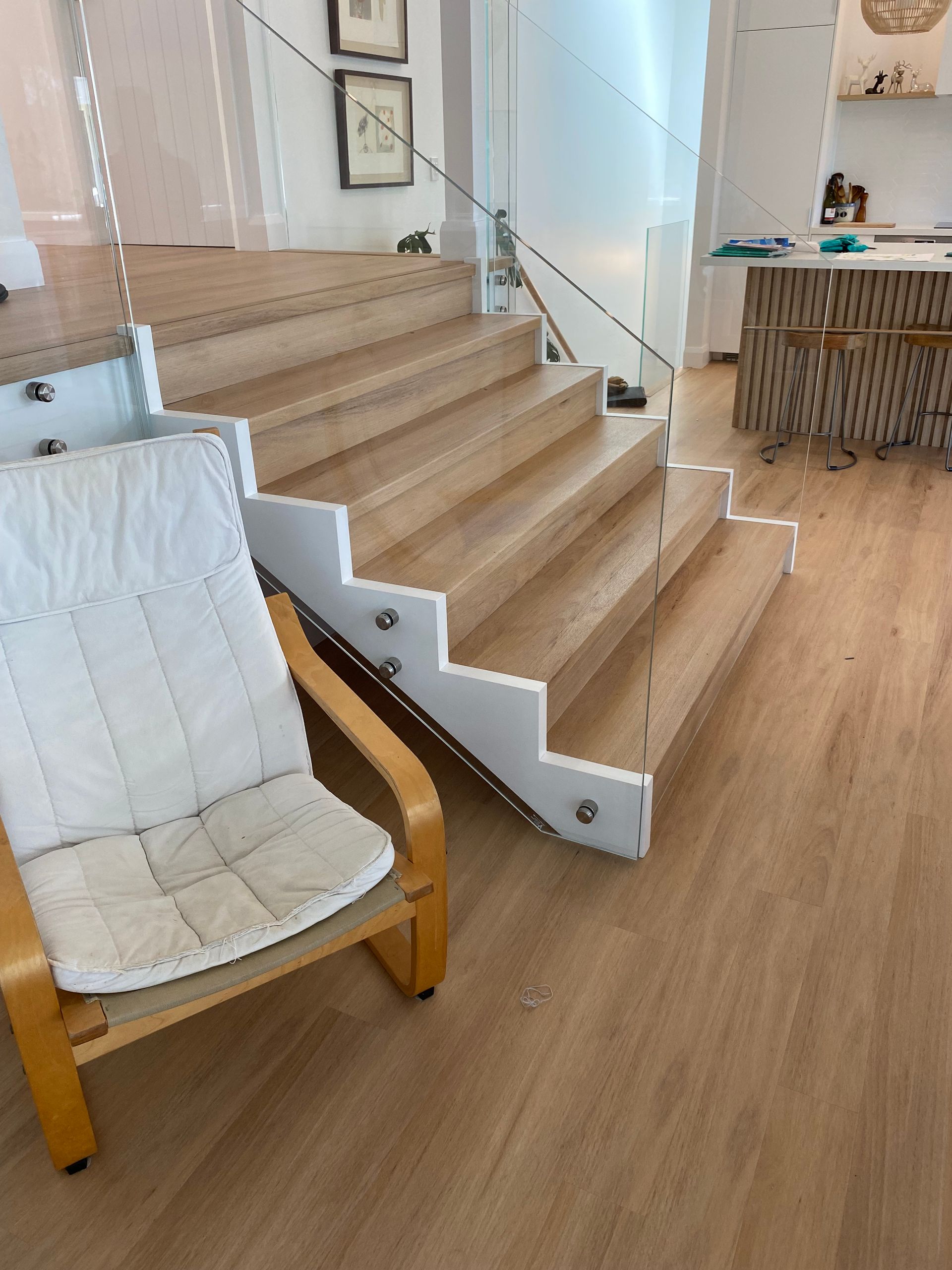 Wooden Staircase With White Trim, Glass Railing, and an Armchair — My Timber Flooring Blinds & Shutters in Erina, NSW