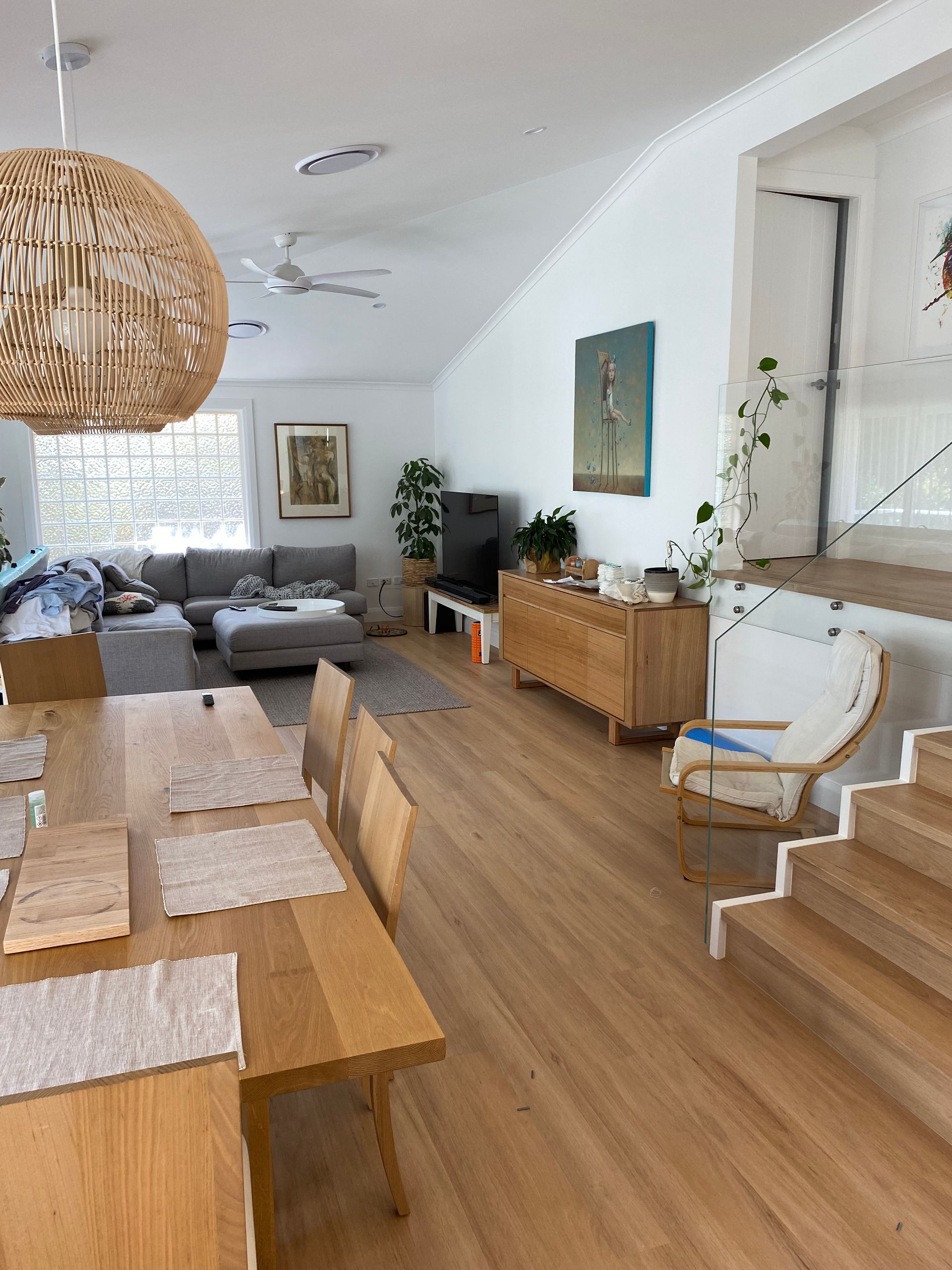 Spacious Living Room With Wooden Floor. Dining Table in Foreground, Sofa, Tv, and Art on White Walls — My Timber Flooring Blinds & Shutters in Erina, NSW