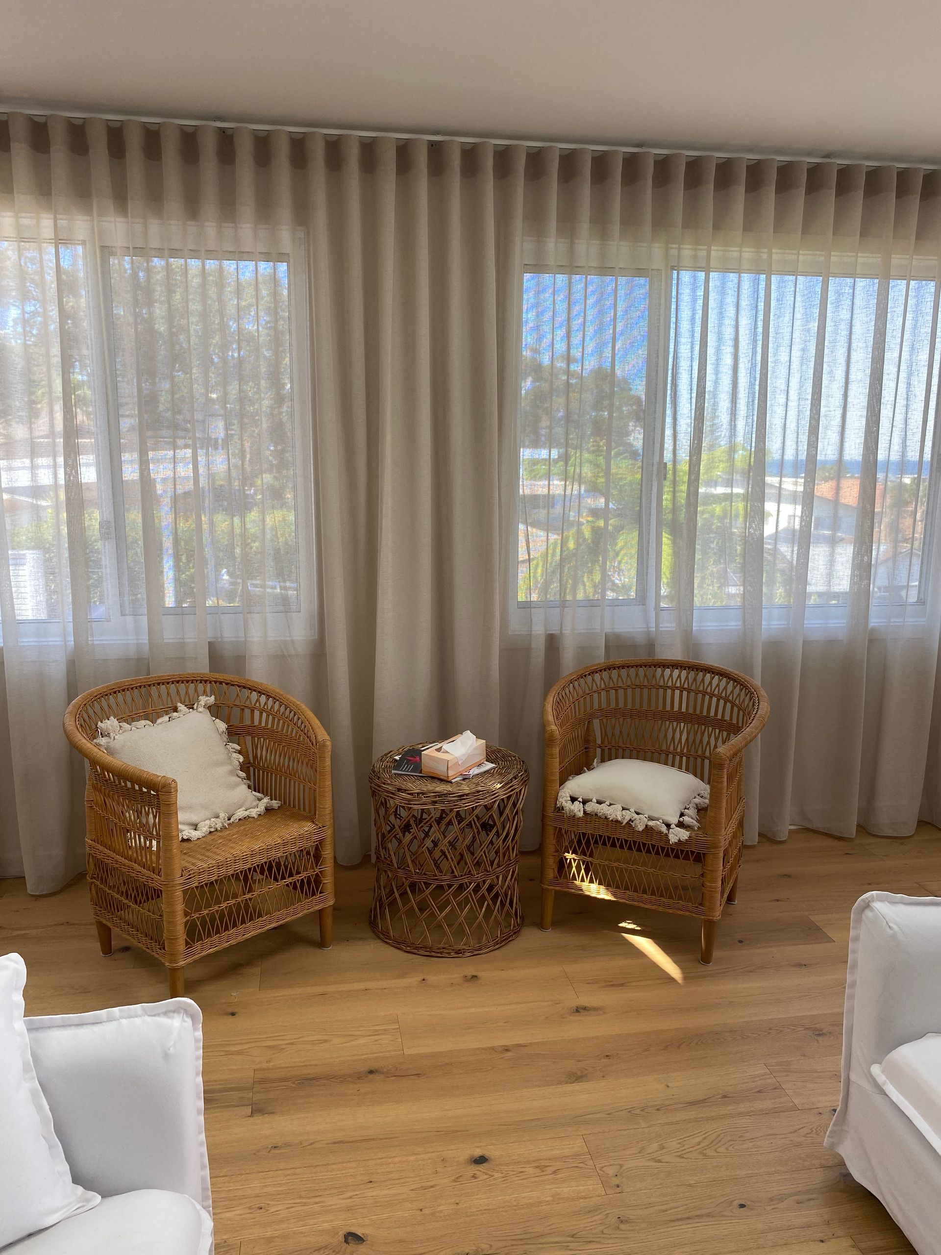 Two Wicker Chairs With Cushions Face Windows With Sheer Curtains; a Small Side Table Stands Between Them — My Timber Flooring Blinds & Shutters in Erina, NSW