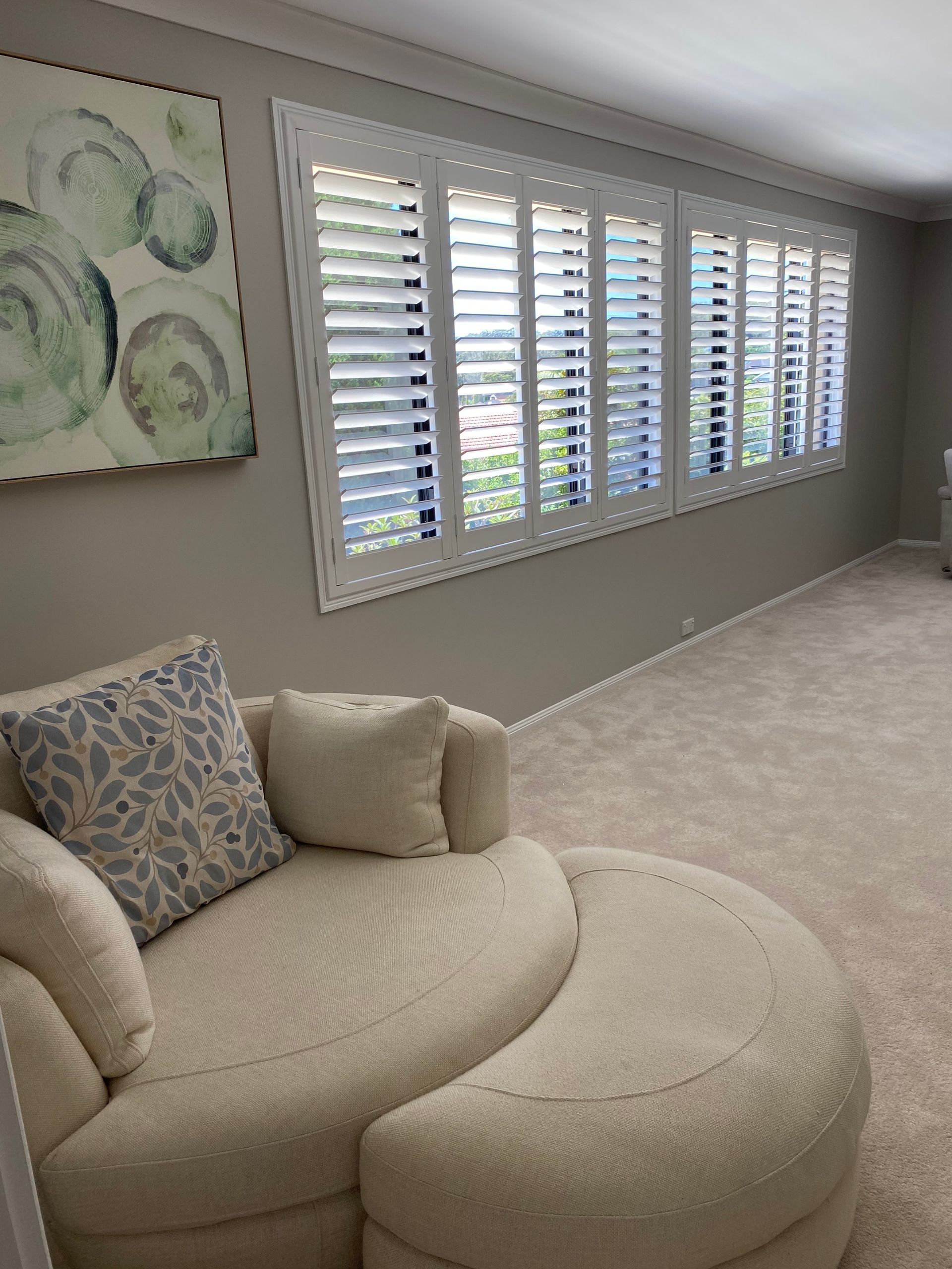 Cozy Living Room With White Shutters, a Curved Cream Couch, and Abstract Art — My Timber Flooring Blinds & Shutters in Erina, NSW