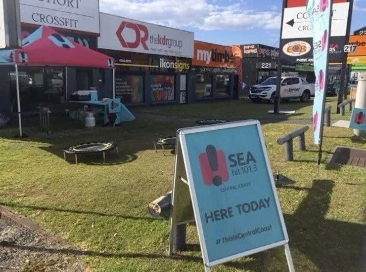 Sign for Sea FM radio station; outdoor promotion. Stores in background — My Timber Flooring Blinds & Shutters in Erina, NSW