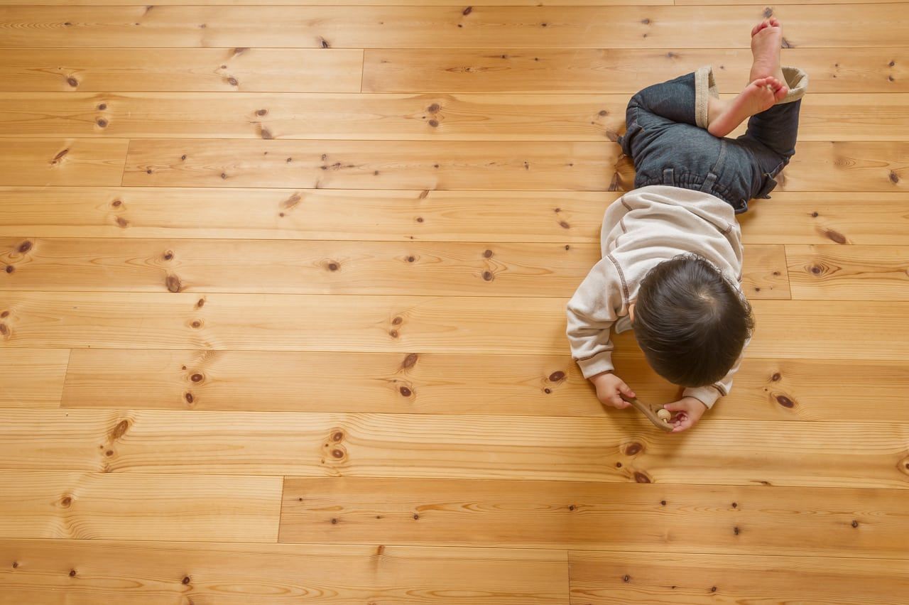 Child Lying on Wooden Floor, Looking Down; Wearing Light Gray Sweater and Dark Blue Jeans — My Timber Flooring Blinds & Shutters in Erina, NSW