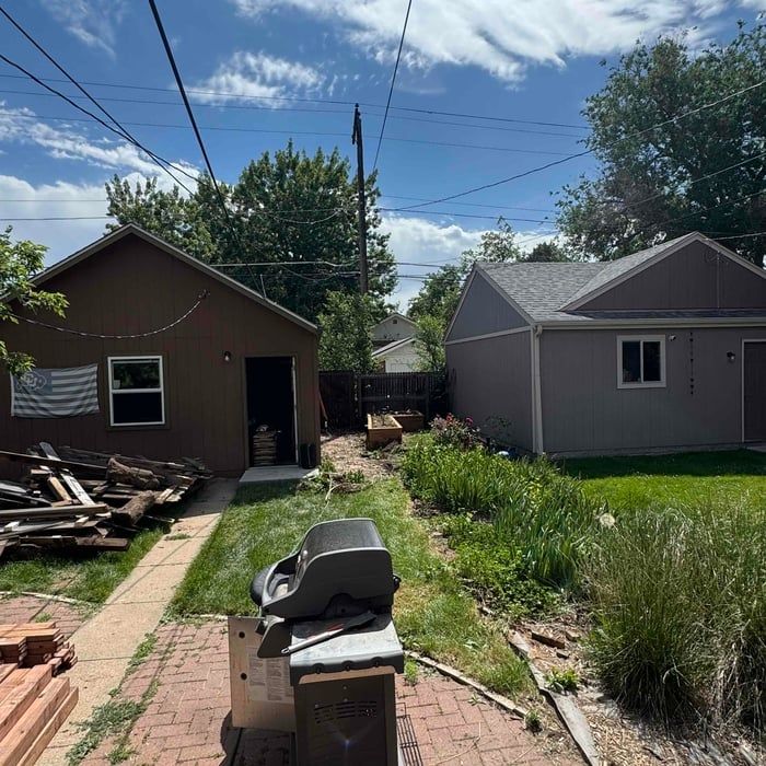 Backyard view with two brown and gray buildings, green grass, and blue sky.
