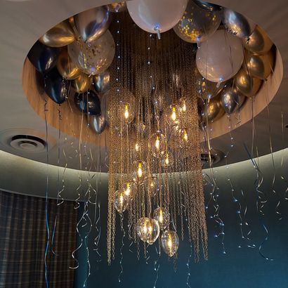 Chandelier surrounded by balloons; silver, gold, and white, hanging from a circular ceiling feature.
