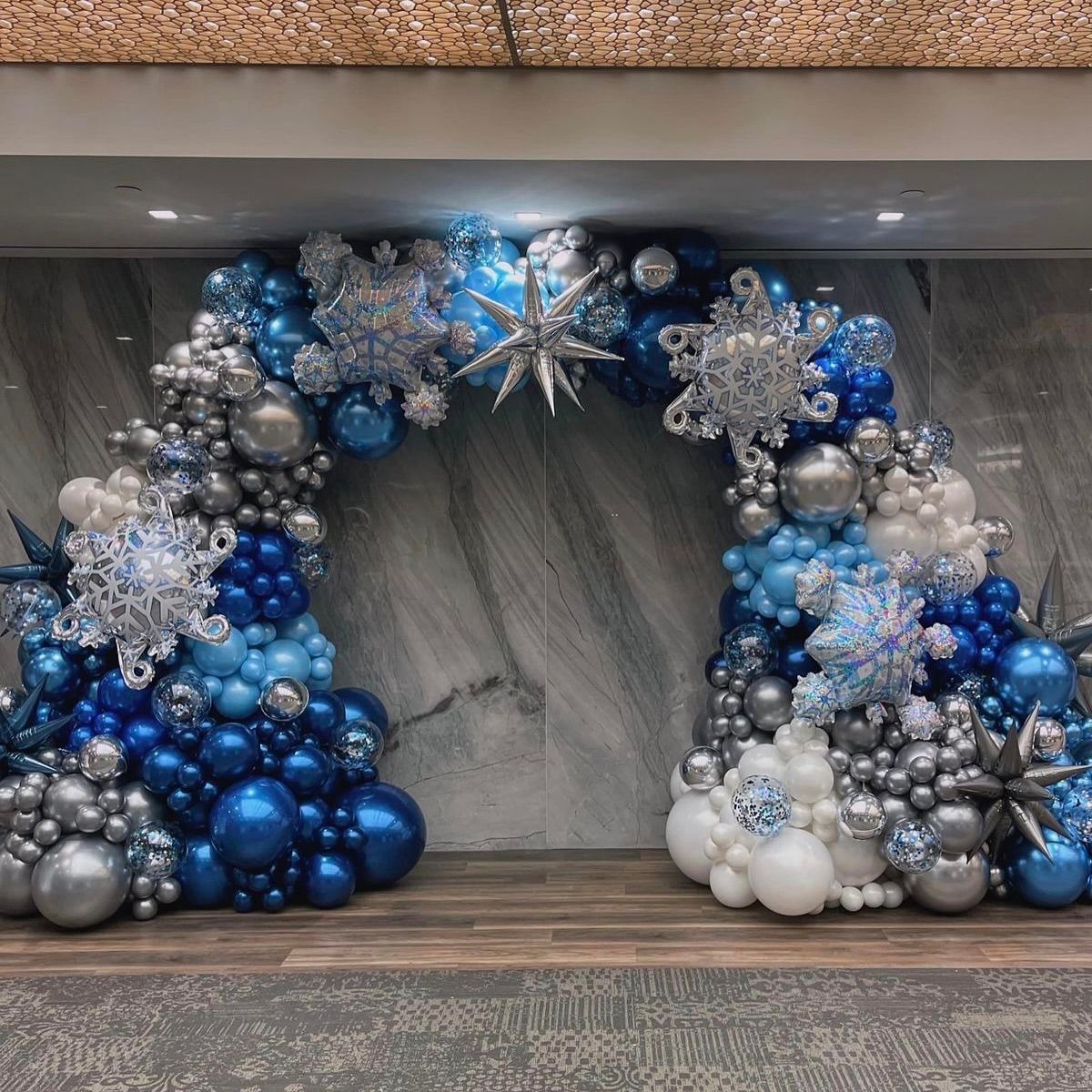 Winter-themed balloon arch in shades of blue, silver, and white, decorated with snowflake accents.