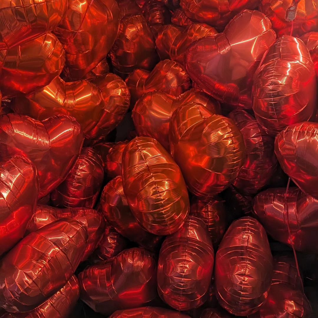 Red and orange heart-shaped balloons, densely packed together, creating a vibrant, festive display.