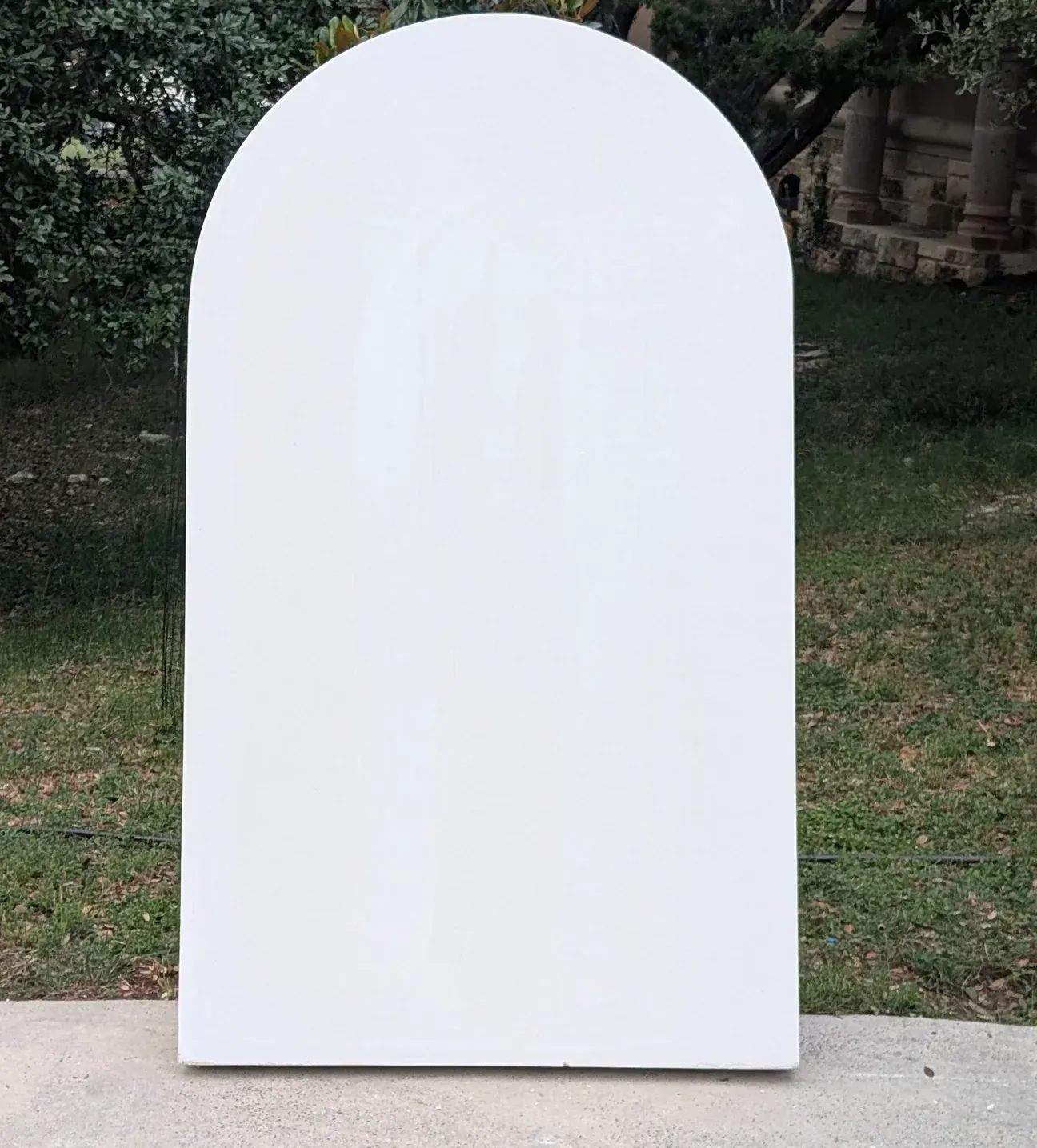 White arched-top panel standing on concrete with grass and foliage in the background.