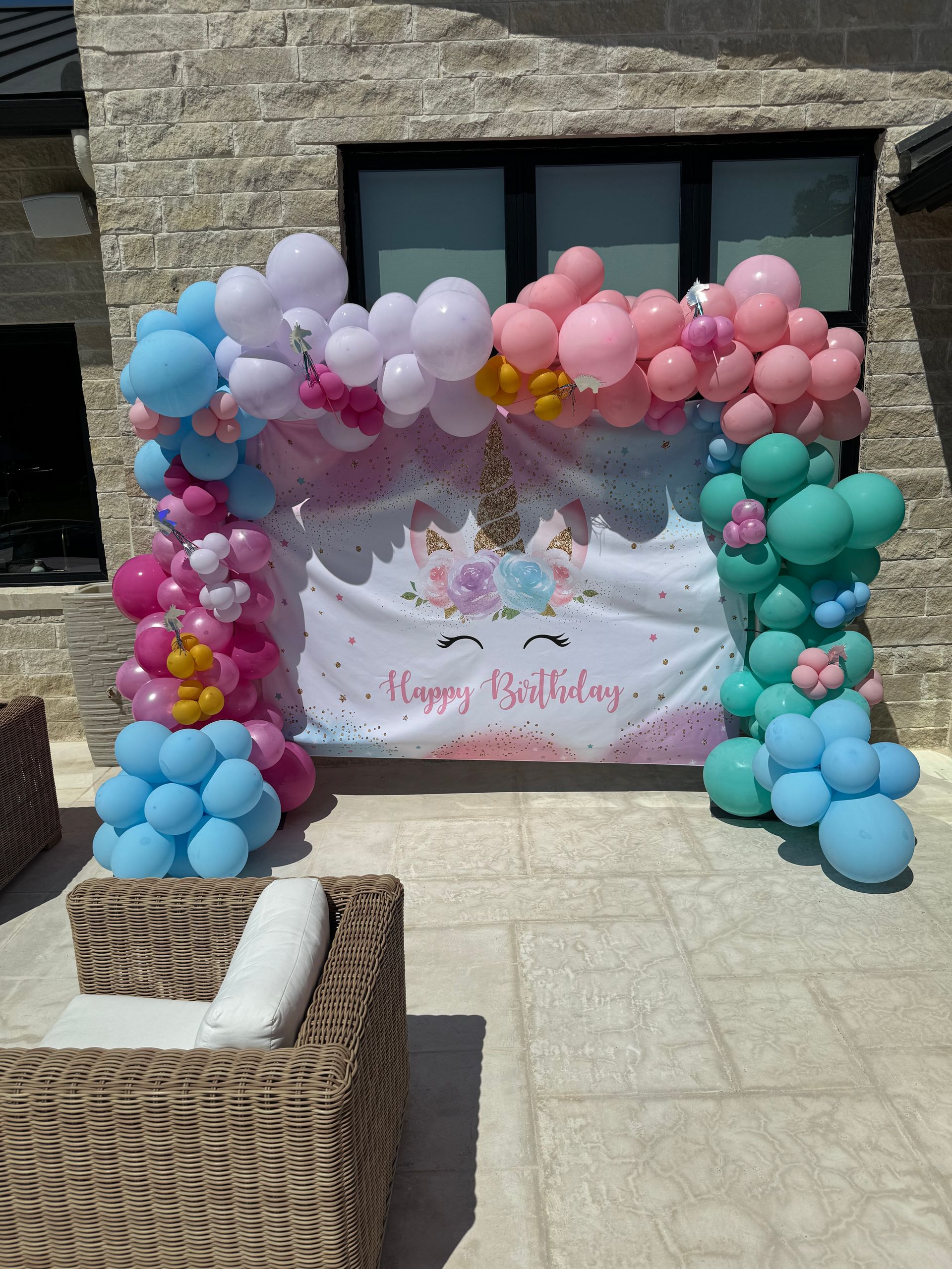Unicorn-themed birthday party backdrop with balloon arch in pink, blue, and green.
