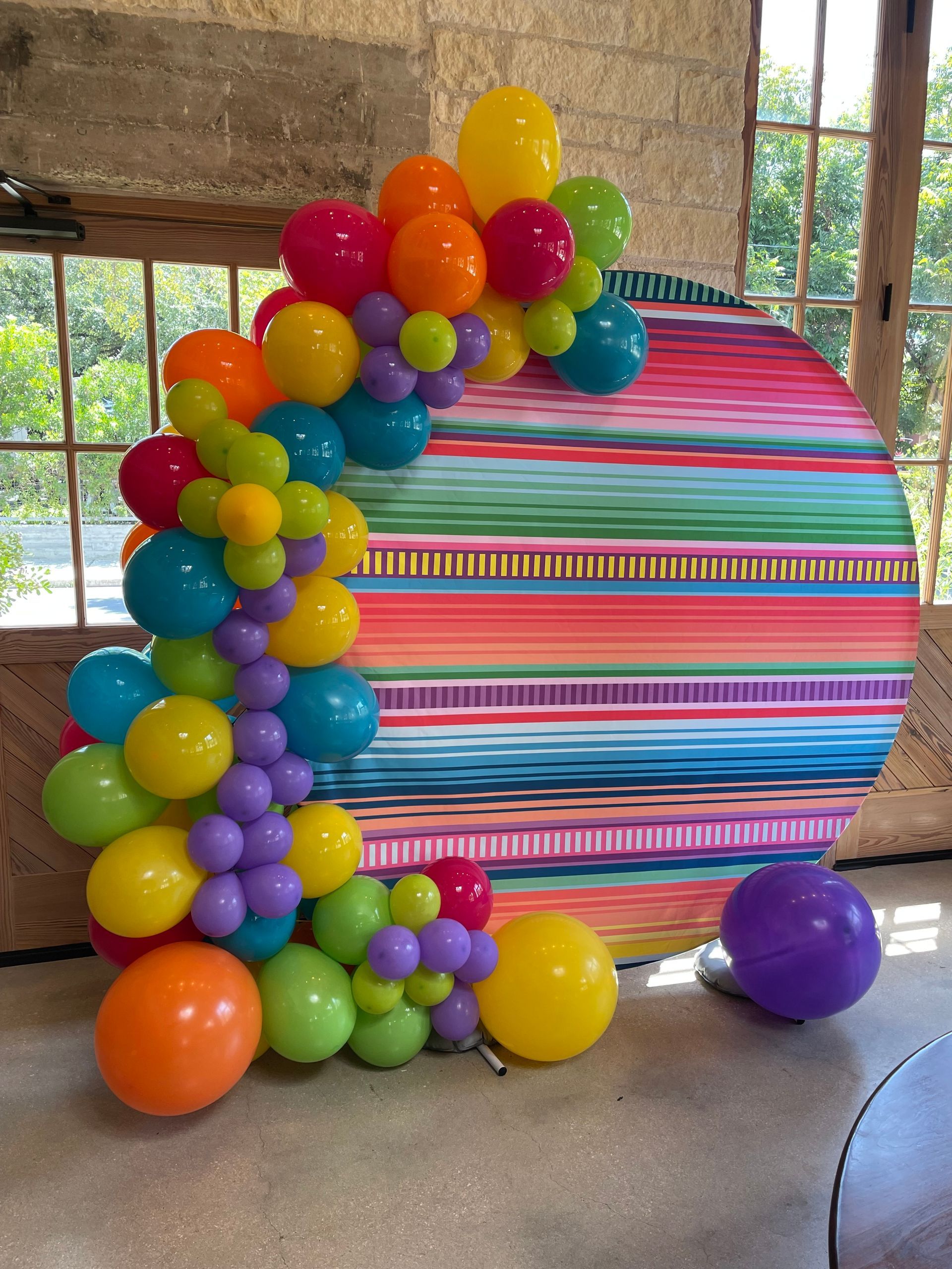 Colorful balloon arch with a striped backdrop, likely for a party.