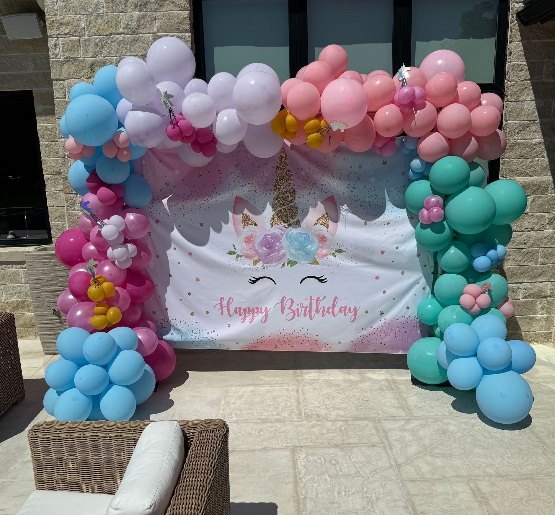 Unicorn-themed birthday backdrop with pink, blue, and white balloons. A banner reads