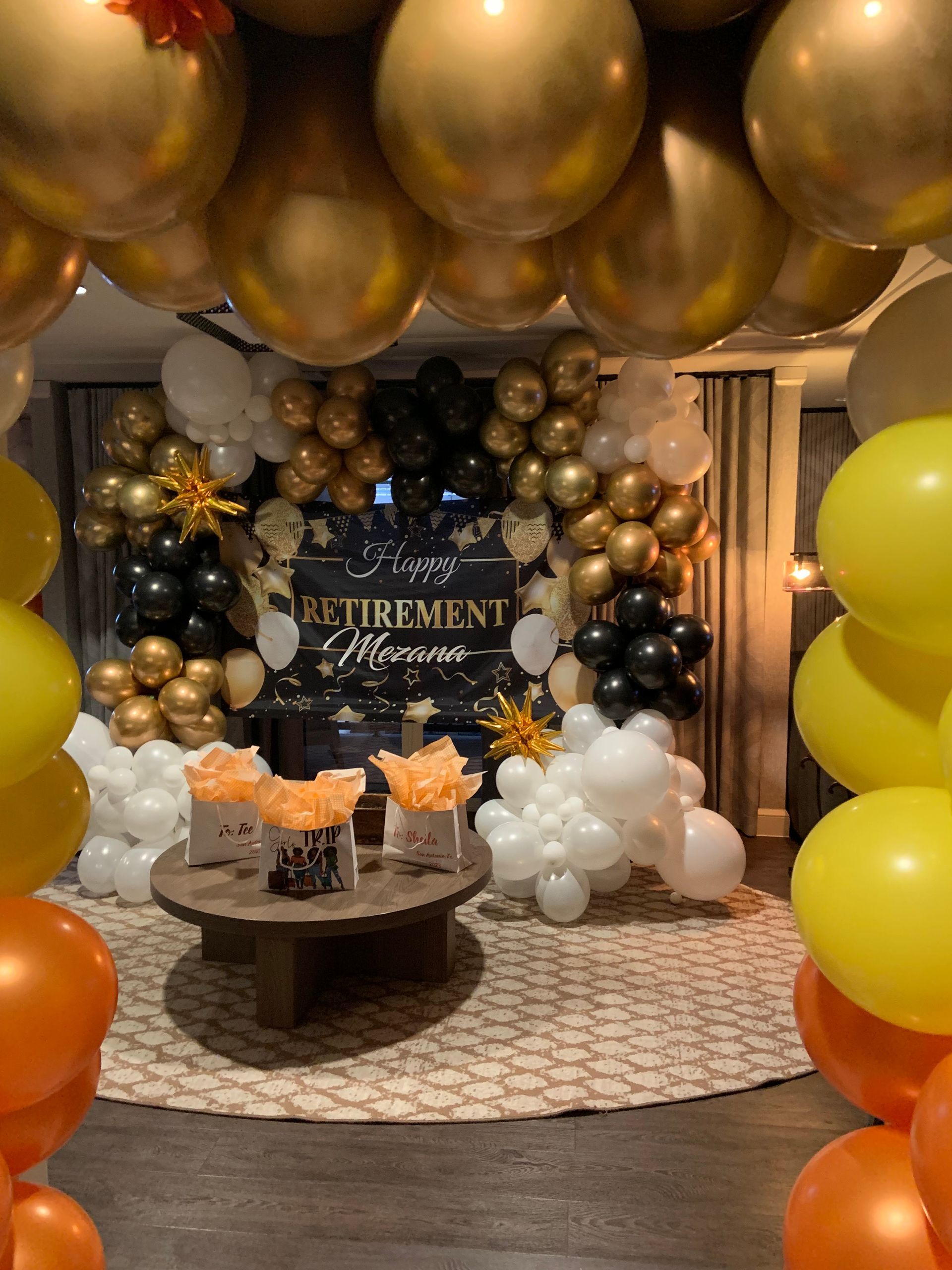 Retirement party: gold, black, and white balloons frame a table with treats.