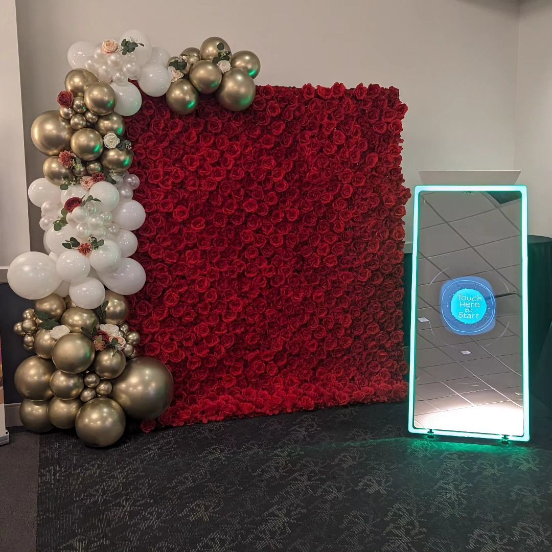 Red floral backdrop with balloon arch, and mirrored photo booth with glowing frame.