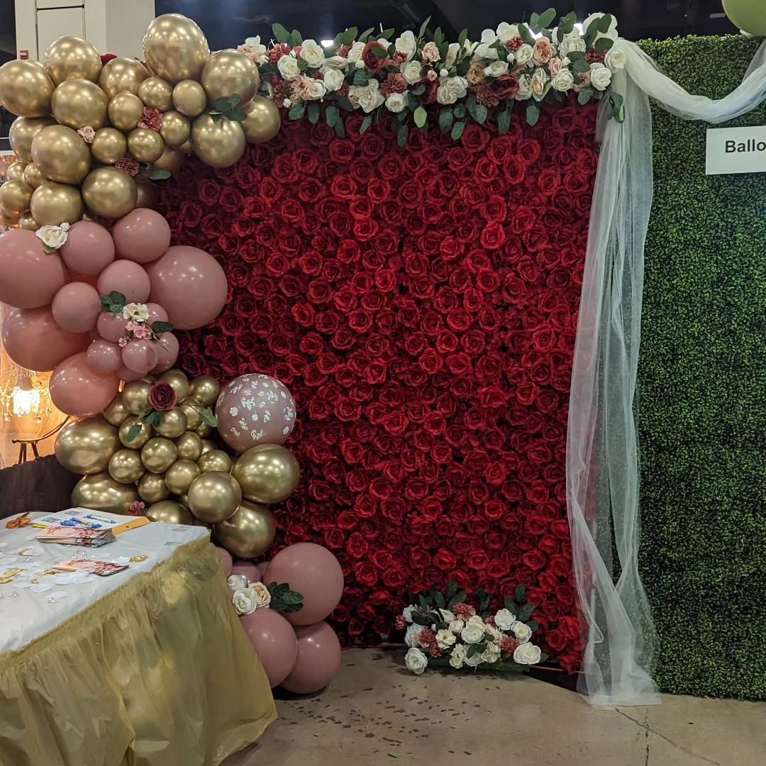 A decorated party backdrop with balloons, red flowers, and greenery.