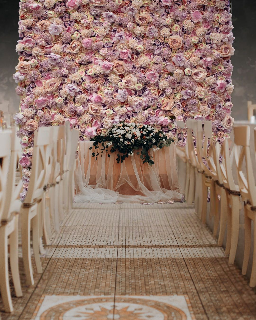 Wedding ceremony aisle with floral wall backdrop and decorated table.