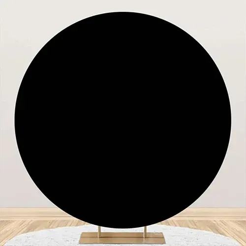 Black circular backdrop on a golden stand, set against a white wall and wooden floor.
