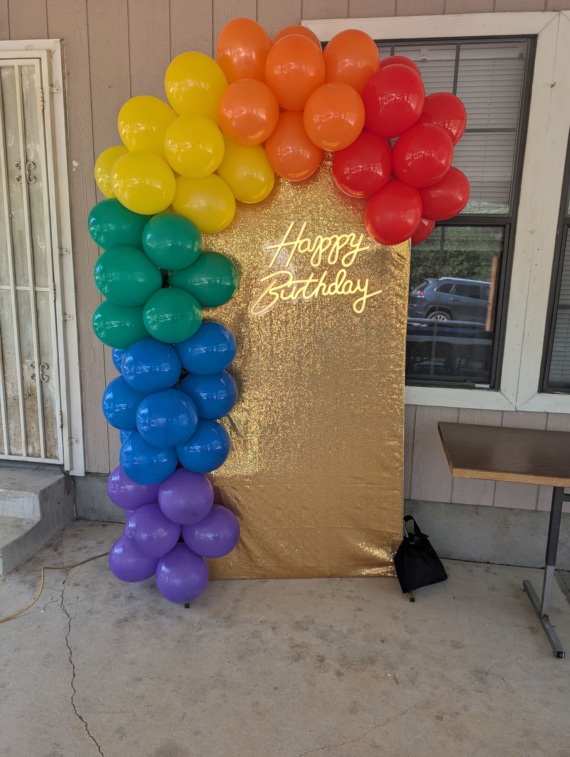 Rainbow balloon arch next to a gold sequin backdrop with
