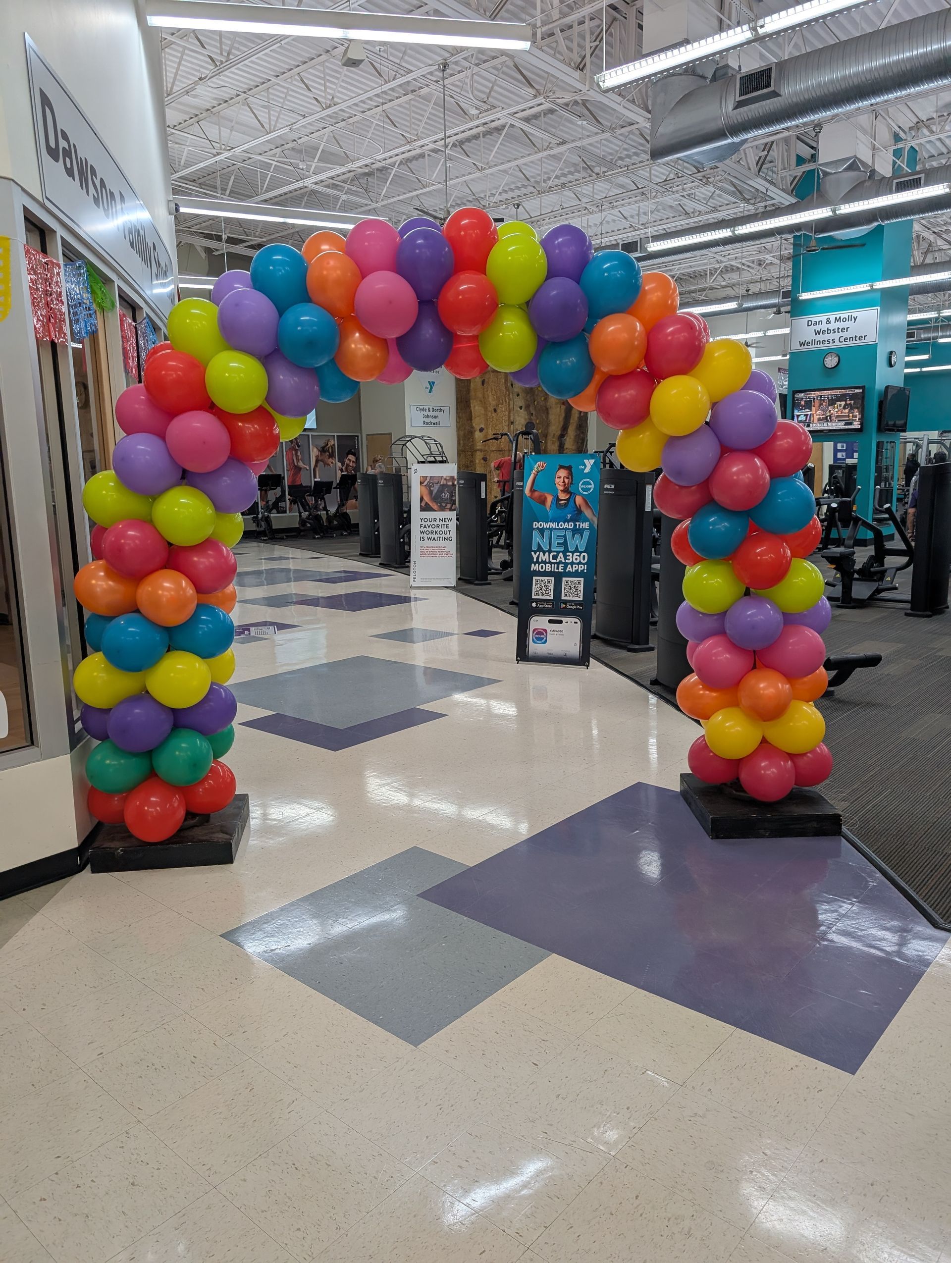 Colorful balloon archway in a store, marking an entrance; red, yellow, green, blue, and purple balloons.