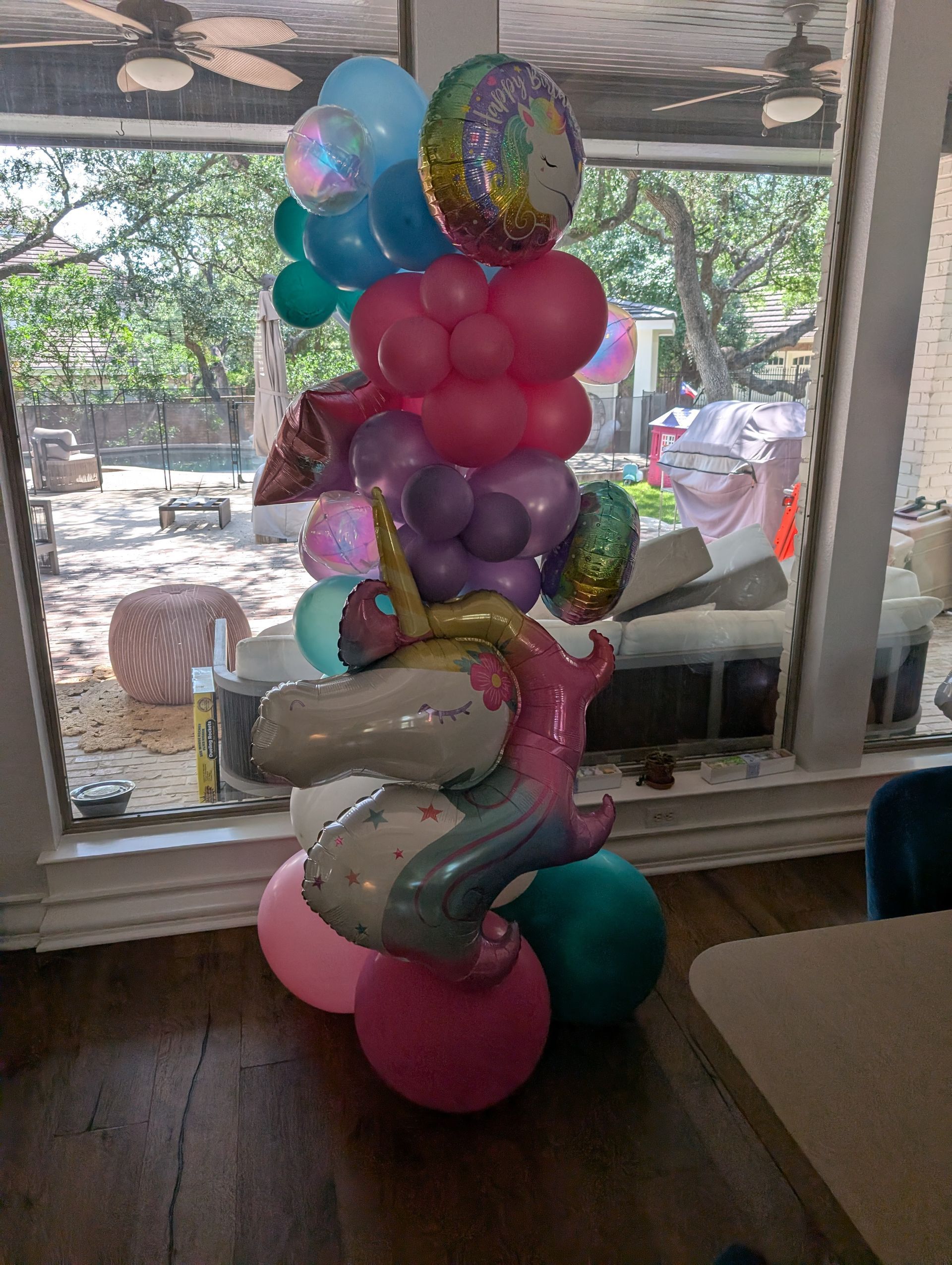 A unicorn balloon sculpture with colorful balloons; indoors by a window.