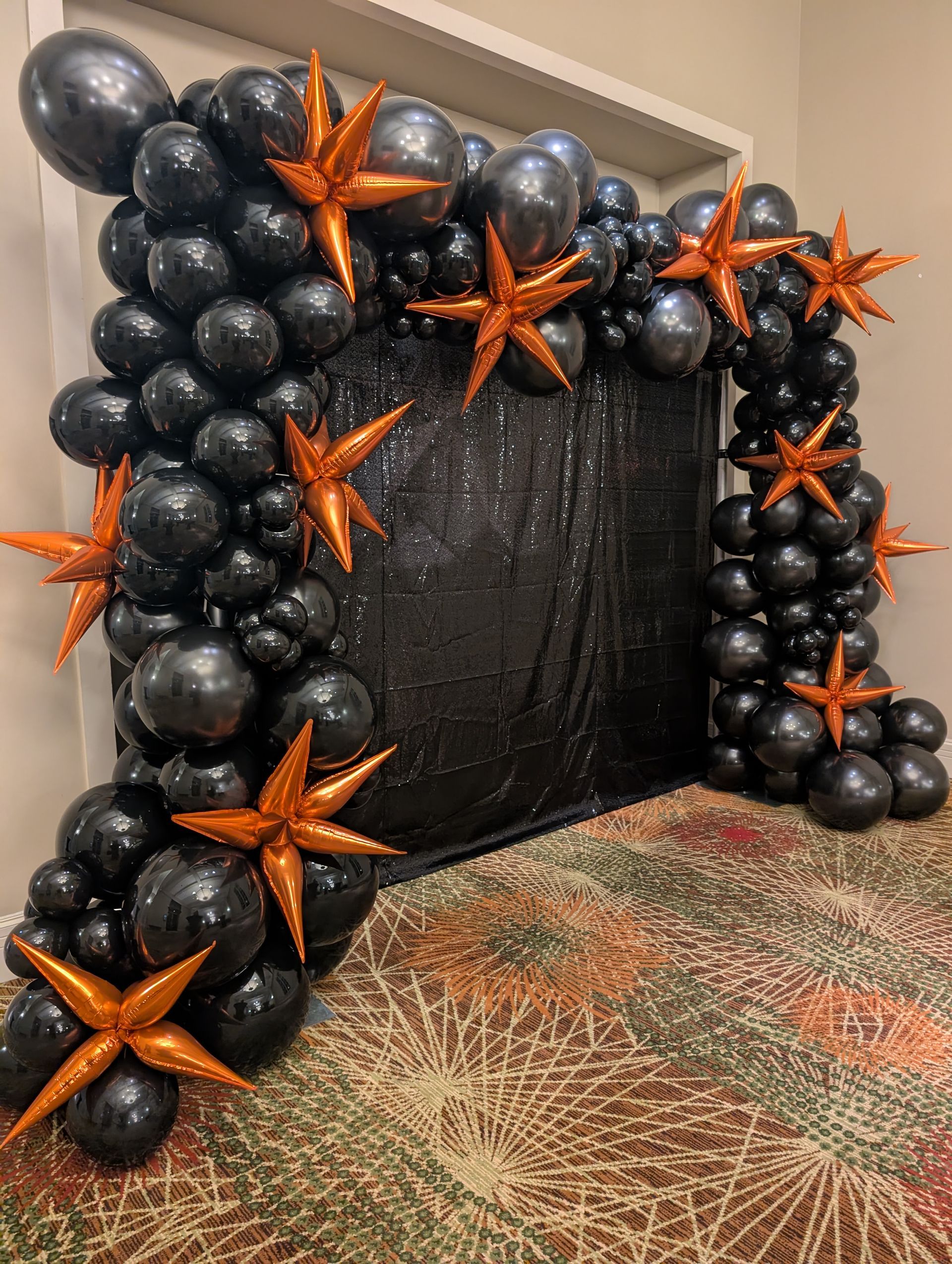 Black and orange balloon arch with star decorations, over a black backdrop.