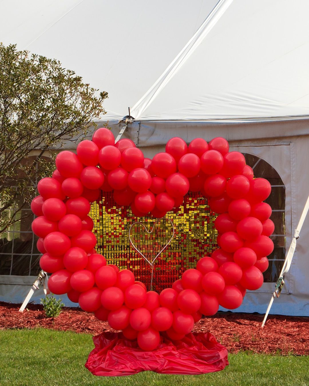 Red balloon heart with gold mosaic center, set on red fabric, in front of a tent.