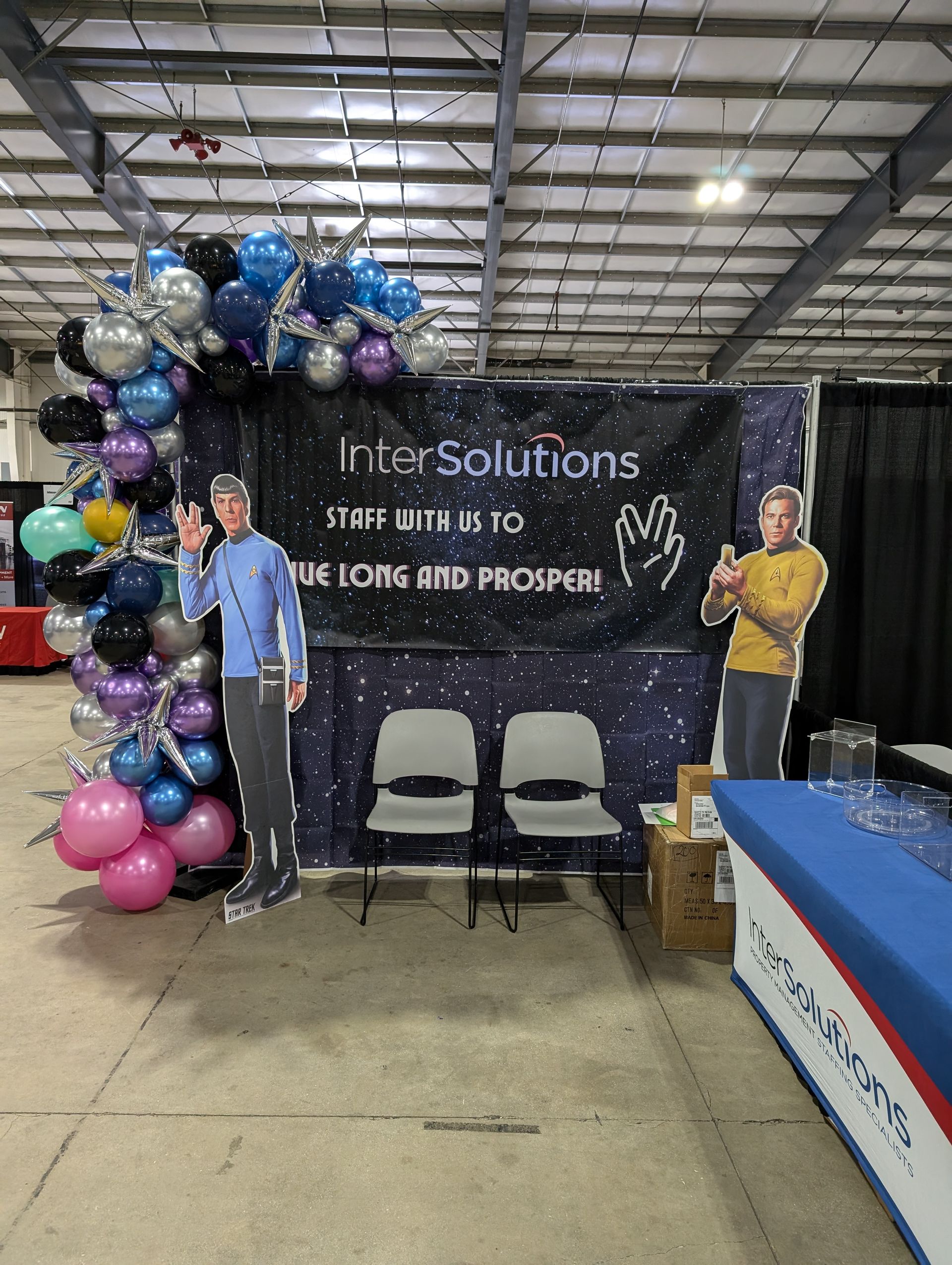 Booth for "InSolutions" with a space theme, featuring cardboard cutouts, balloons, and chairs at an event.