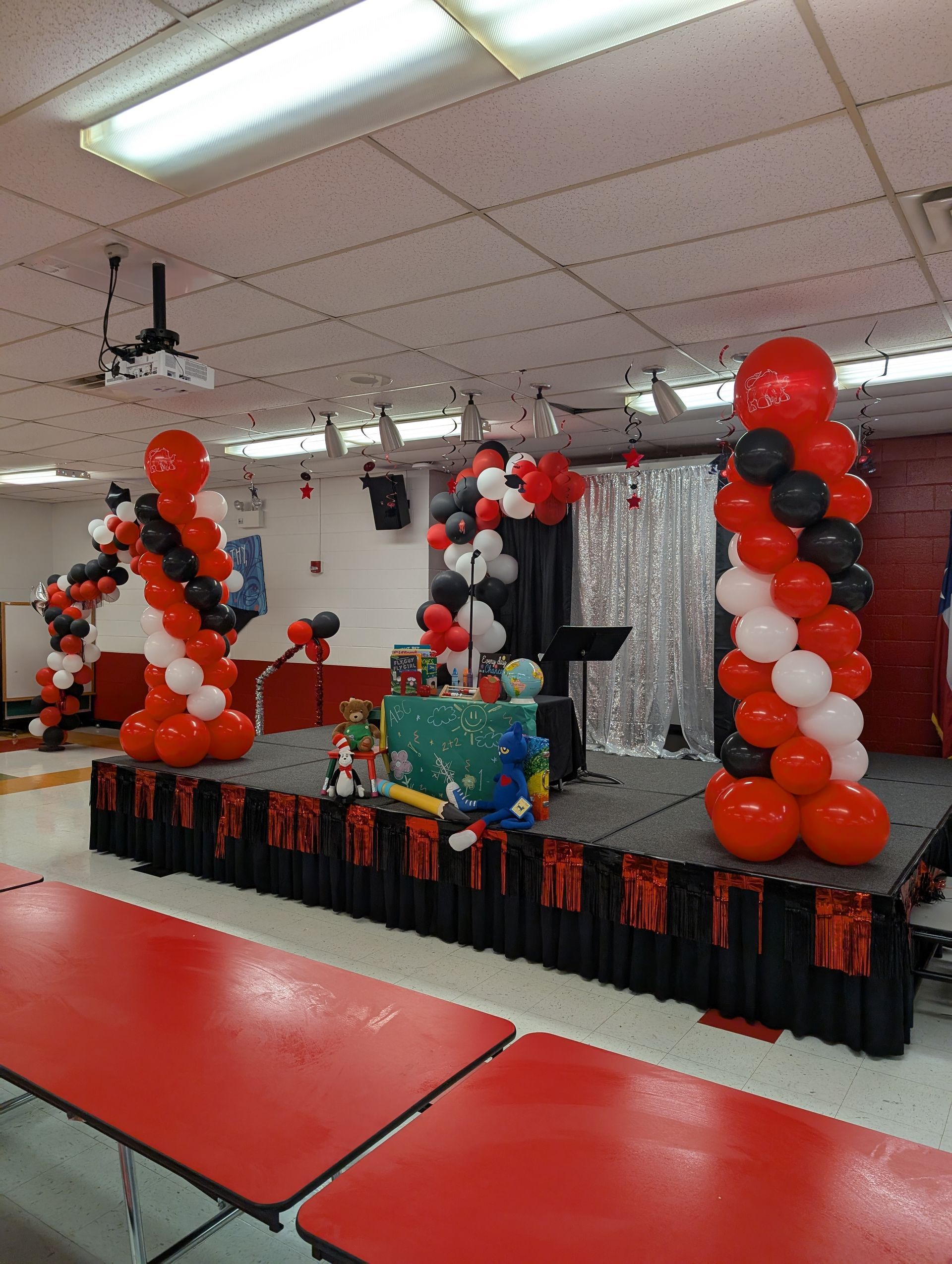 Red, black, and white balloon decorations on a stage with a table. Red tables in the foreground.