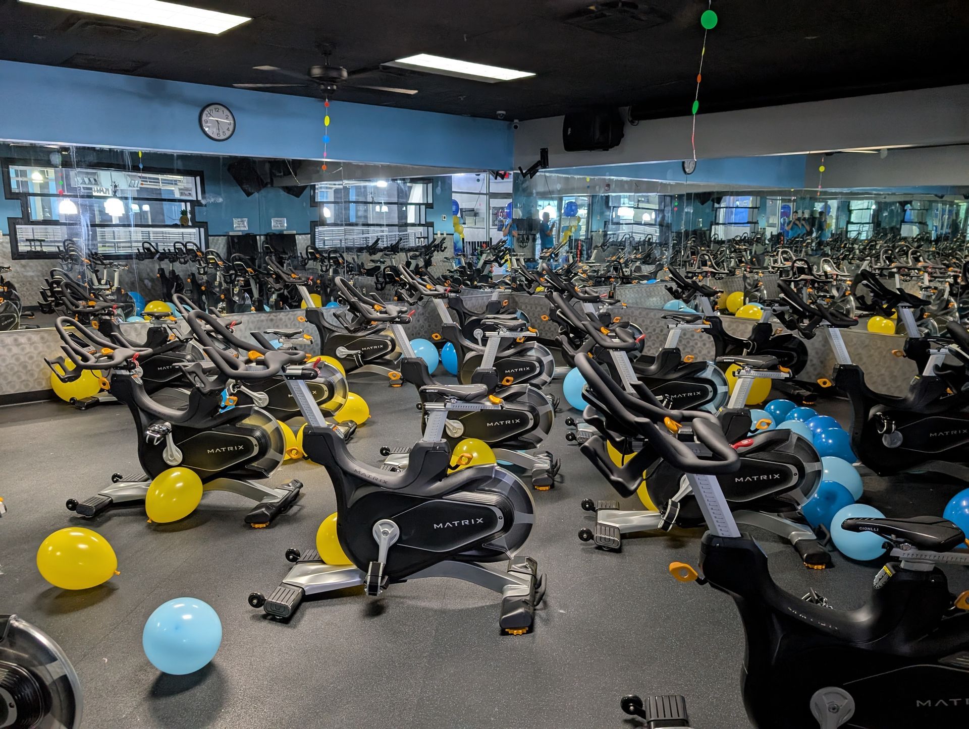 Indoor cycling studio with many stationary bikes, decorated with blue and yellow balloons.