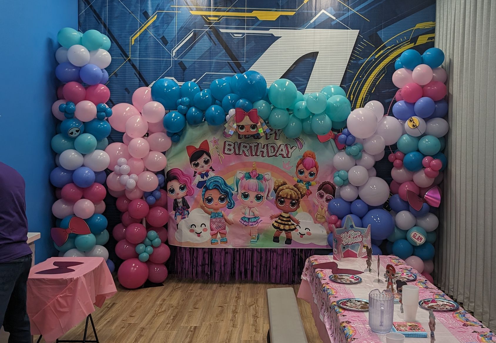Party scene with colorful balloon decorations and a banner featuring cartoon characters. Table set for a party.