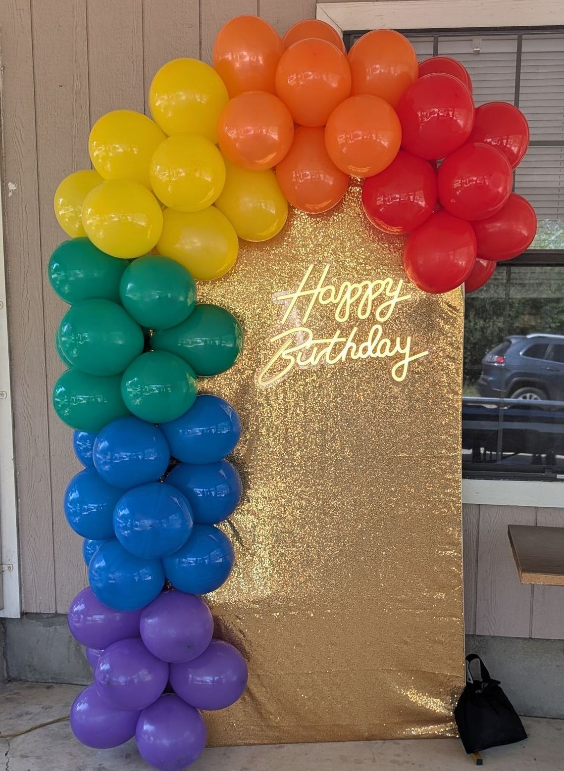 Rainbow balloon arch with a gold sequin backdrop that reads "Happy Birthday".