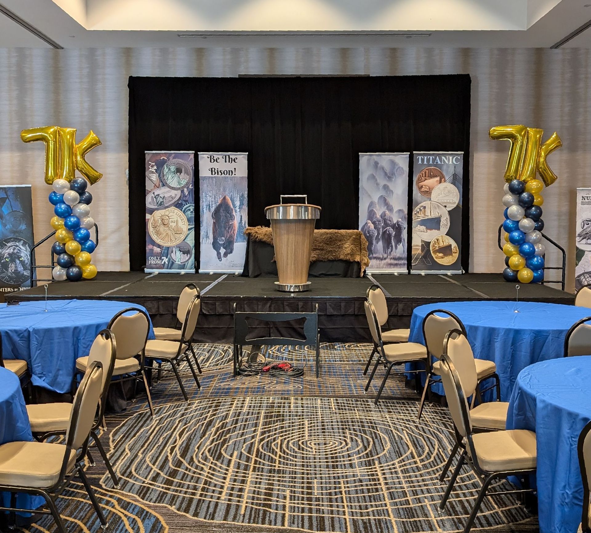 Event stage with banners, podium, balloon decorations, and round tables set for attendees.