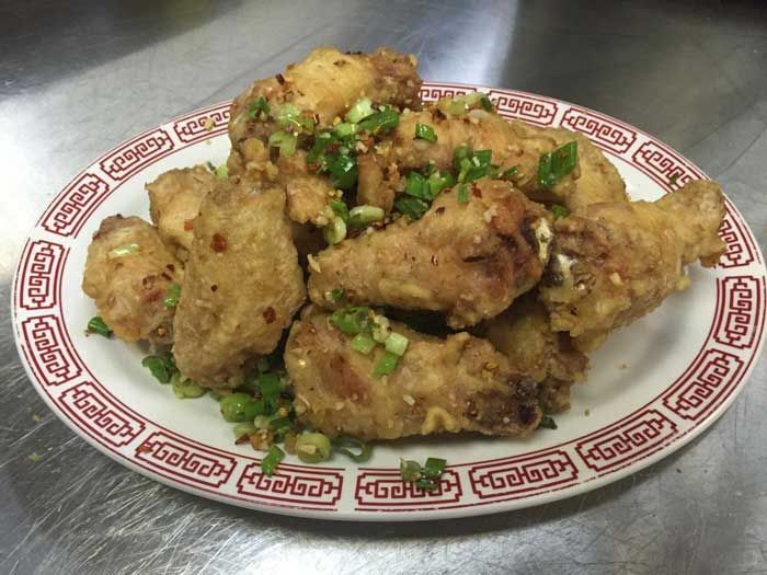 Un plato de alitas de pollo fritas con cebollas verdes sobre una mesa.