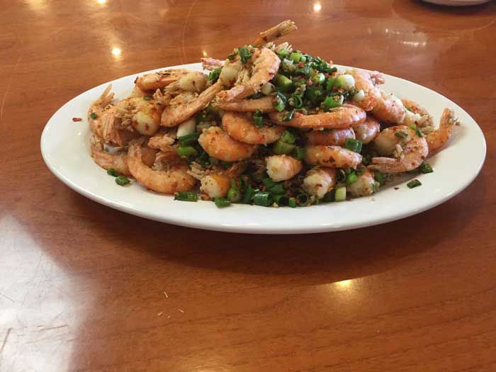 Un plato blanco cubierto con camarones y cebollas verdes sobre una mesa de madera.