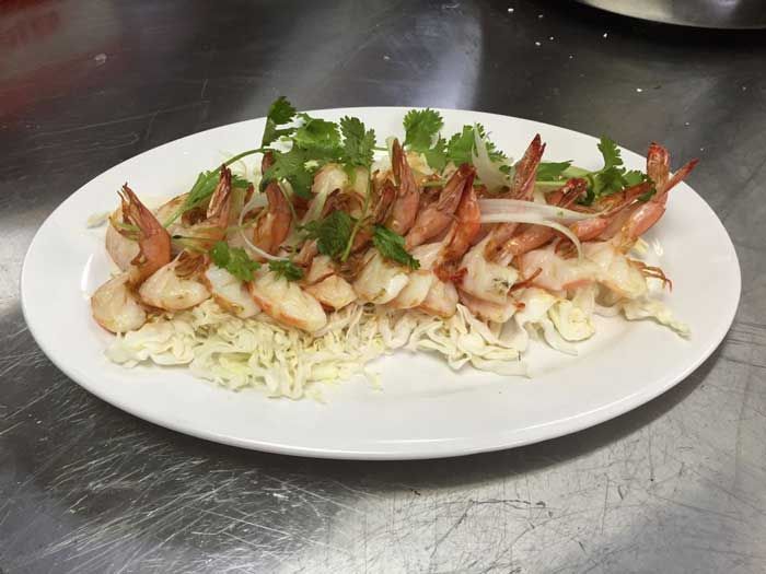 Un plato blanco cubierto con camarones y repollo sobre una mesa.
