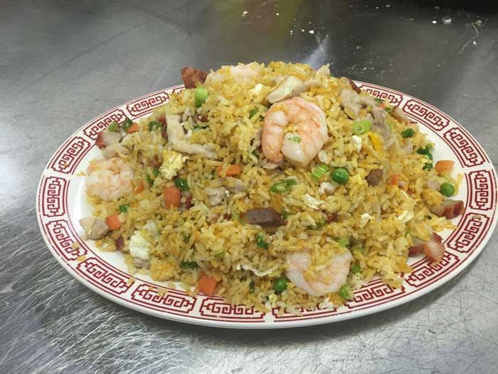 Un plato de arroz frito con camarones y verduras en una mesa.