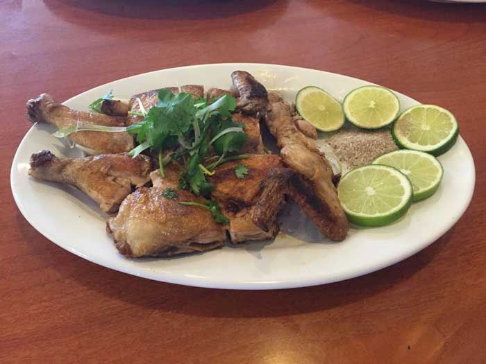 Un plato blanco cubierto con pollo y limas sobre una mesa de madera.
