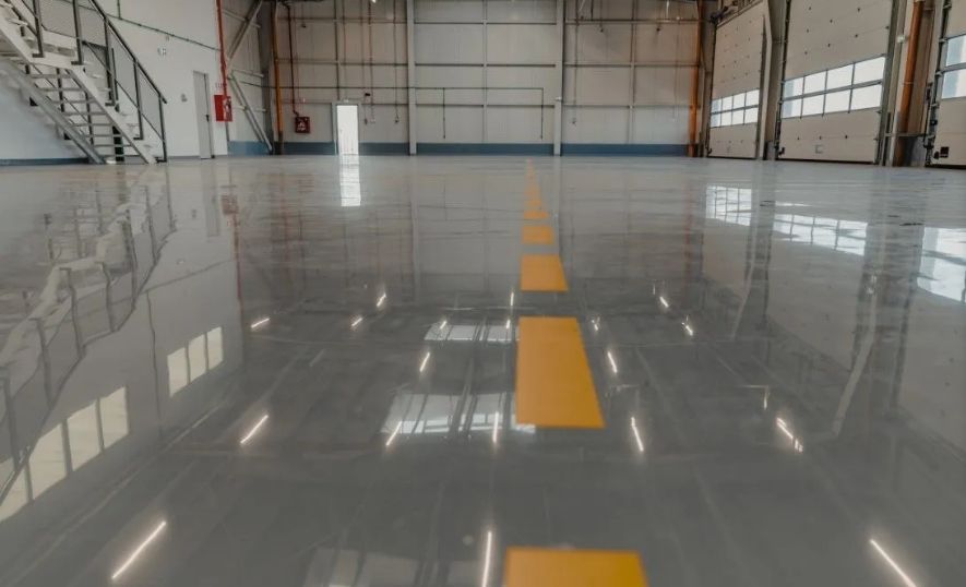 Shiny grey commercial epoxy floor in a large warehouse with yellow lines.