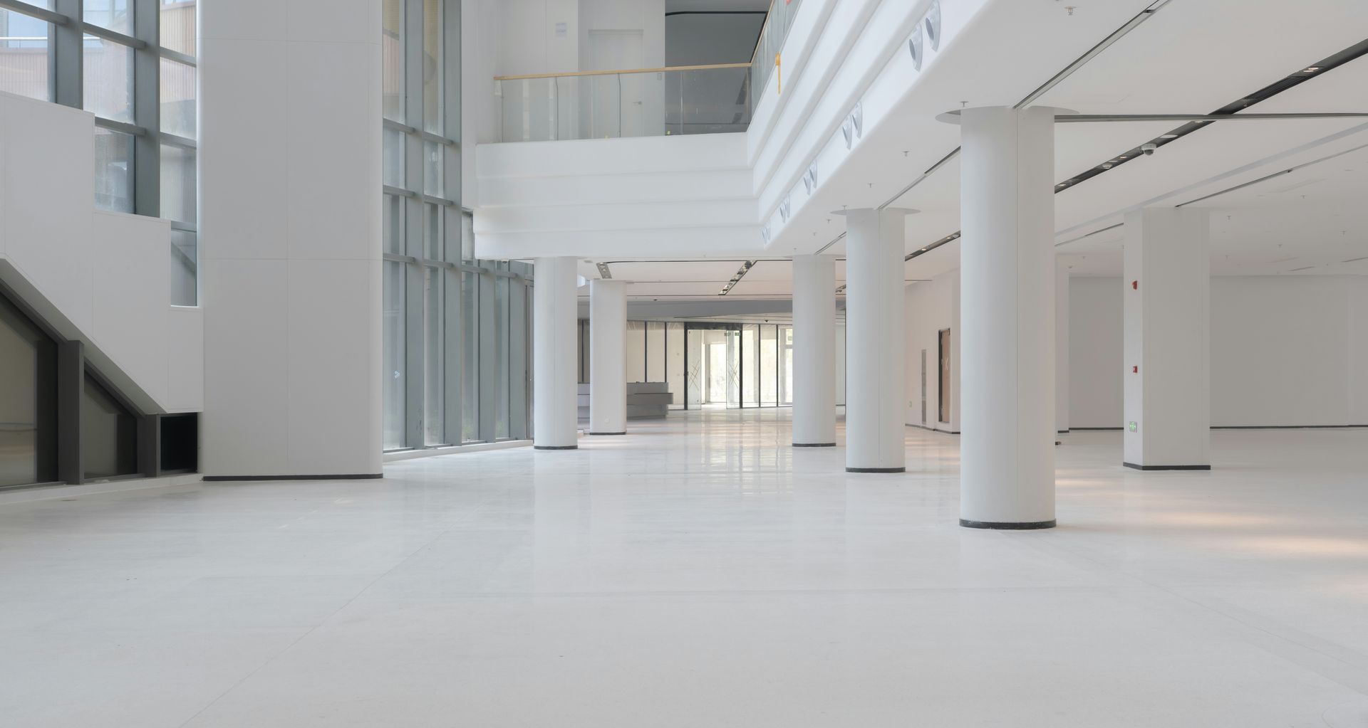 A bright, minimalist office lobby with white floors, white columns, and floor-to-ceiling windows.