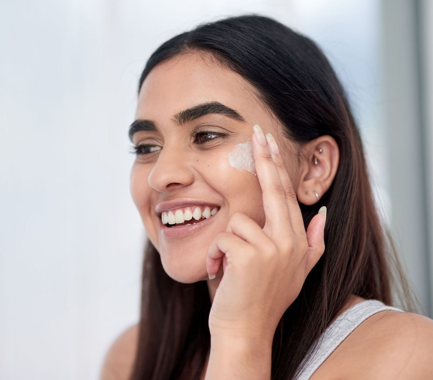 a woman is smiling while applying cream to her face
