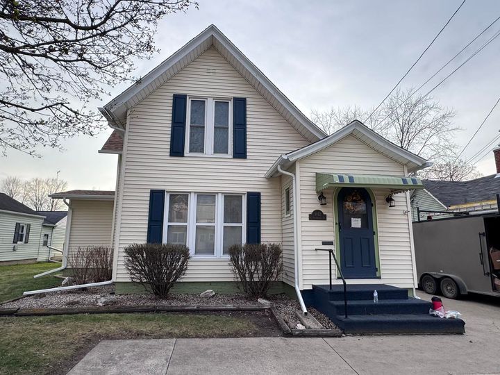 Two-story beige house with blue shutters and front porch in a suburban neighborhood