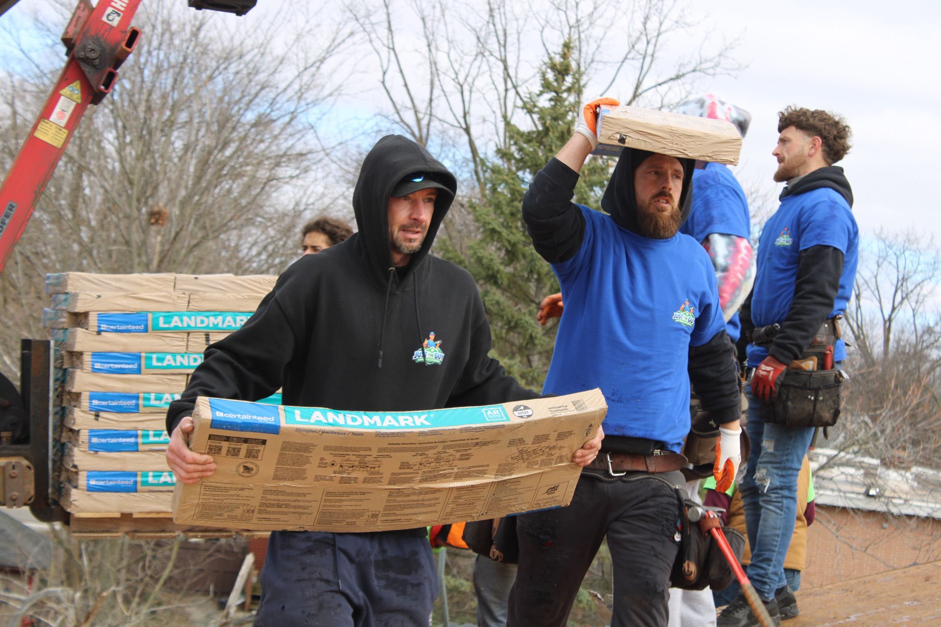 Workers in hoodies carry stacked bricks at an outdoor construction site.