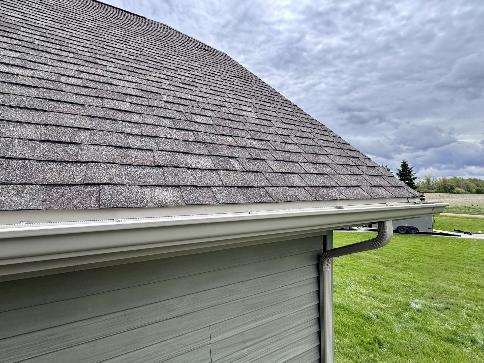 Close-up of a house roof and white gutter above green lawn under a cloudy sky