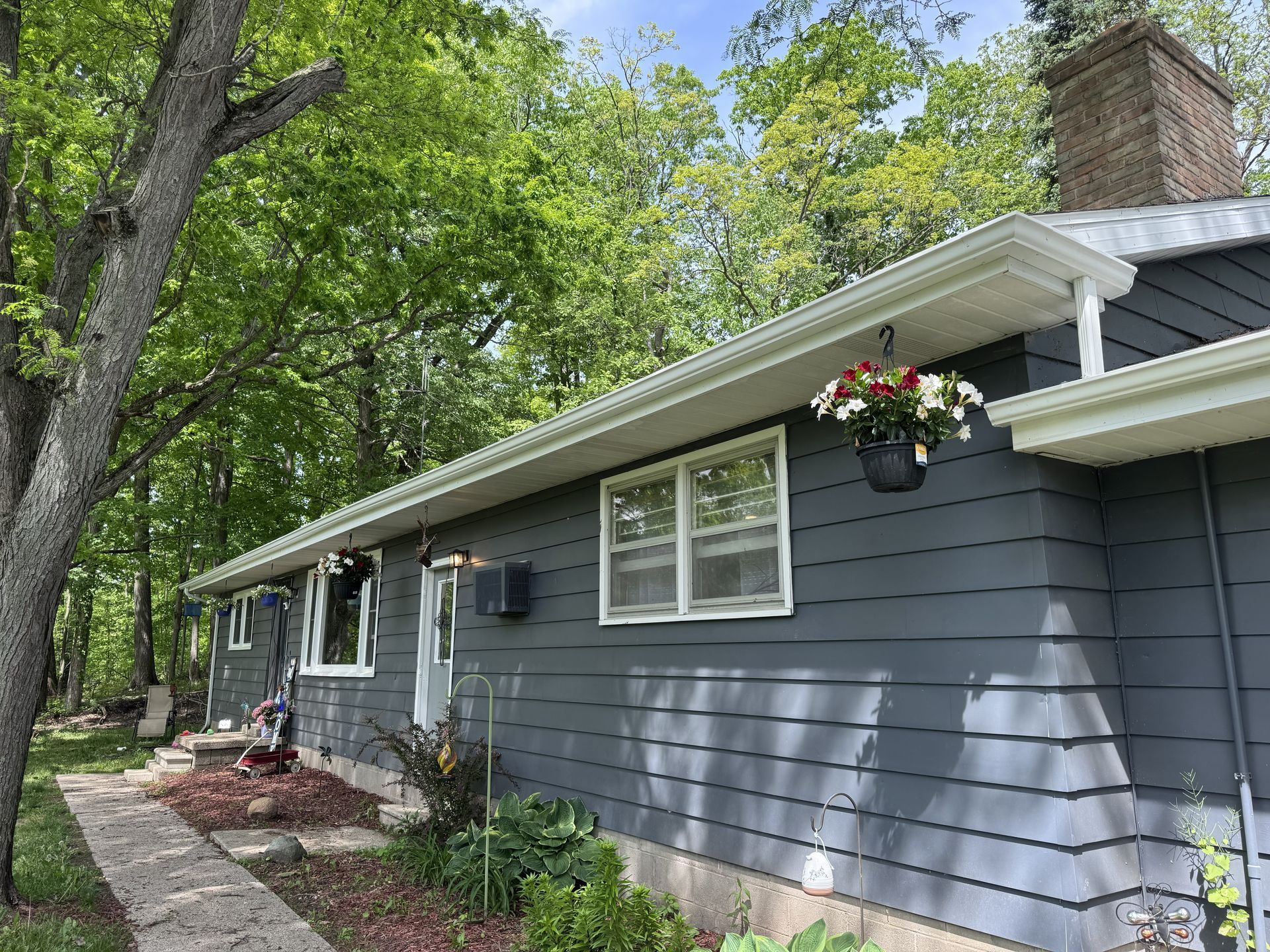 Gray house exterior with white trim, flower baskets, and a tree-lined front yard