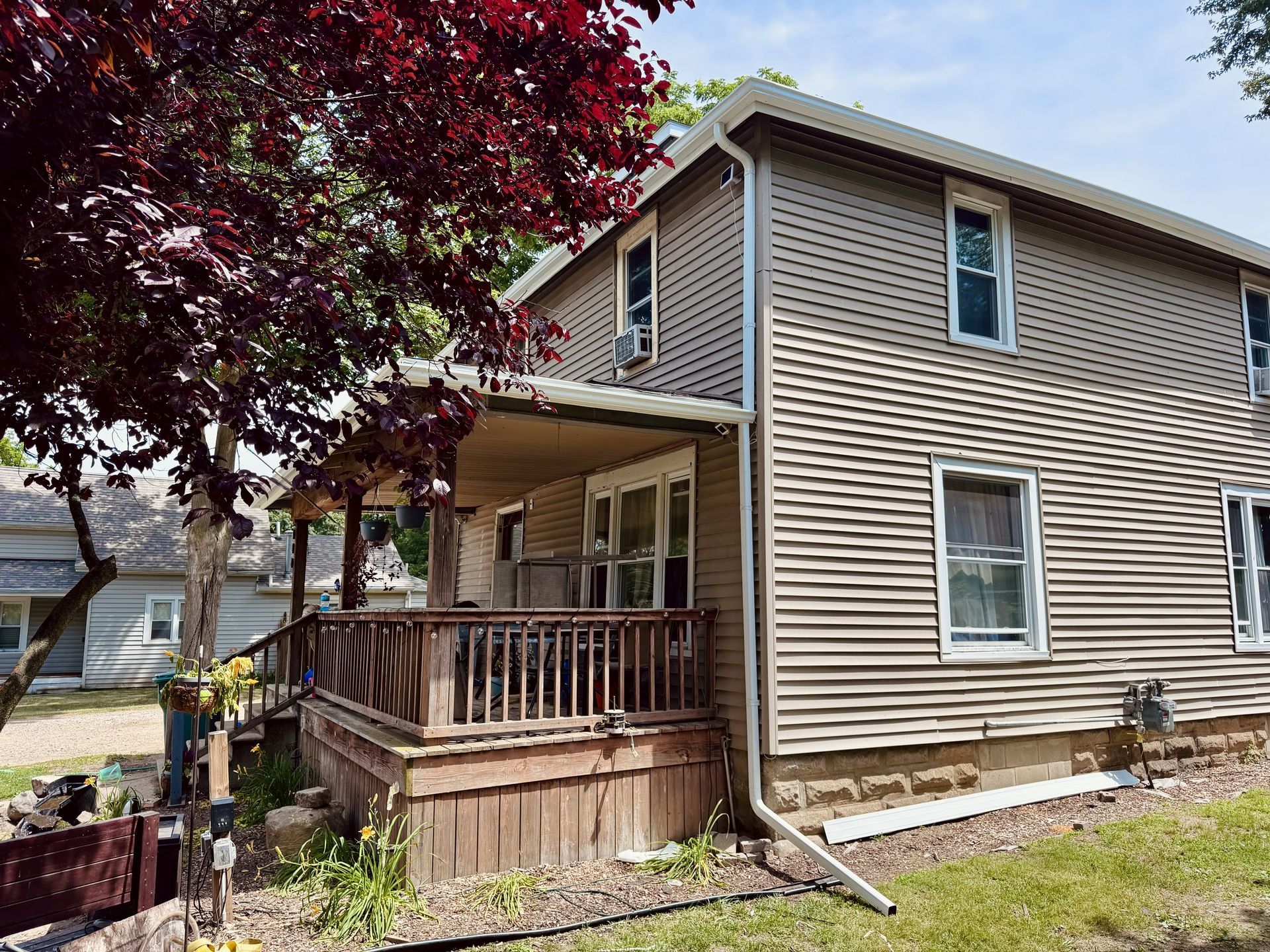 Two-story tan house with a covered porch and red-leafed tree in front
