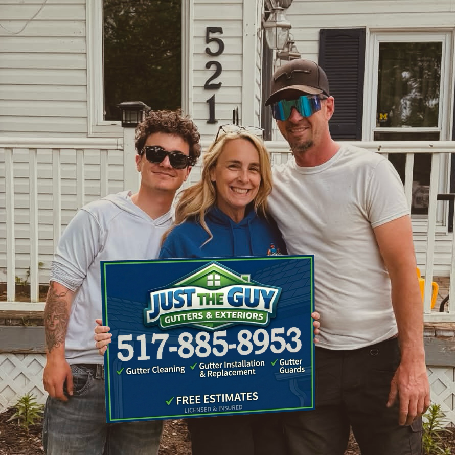 Three people holding a “Just the Guy” sign in front of a house